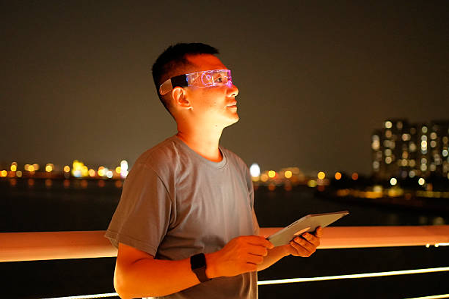 Person using tablet and glowing glasses at night