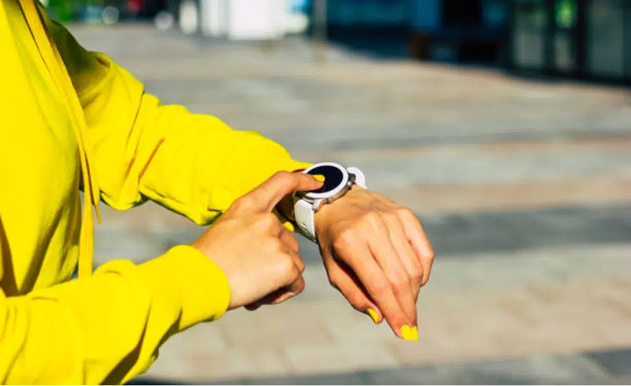 Person using smartwatch outdoors in yellow hoodie